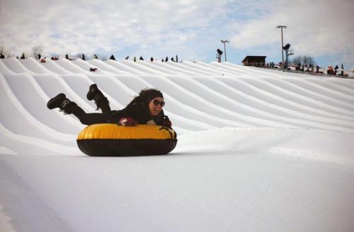 A person joyfully sledding down a snowy slope on a yellow inflatable tube, surrounded by a winter landscape.