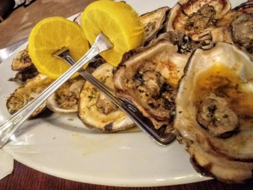 A plate of grilled oysters garnished with lemon wedges and served with forks.