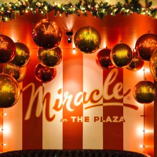 A festive wall with red and white stripes, adorned with large gold and red ornaments and twinkling lights.