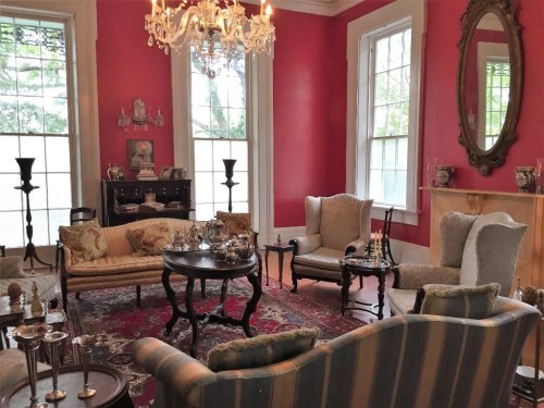 A cozy living room with pink walls, elegant furniture, a chandelier, and large windows letting in natural light.