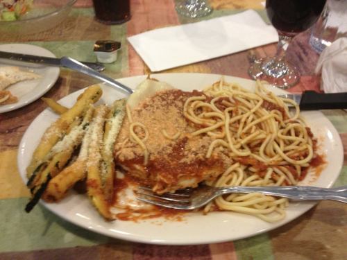 A plate of lasagna with spaghetti and marinara sauce, served with seasoned zucchini fries on the side.