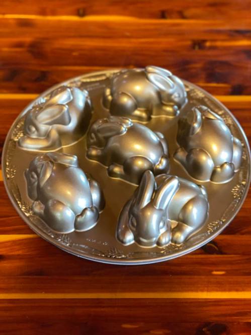 A silver rabbit-shaped mold with six cavities, resting on a wooden surface.