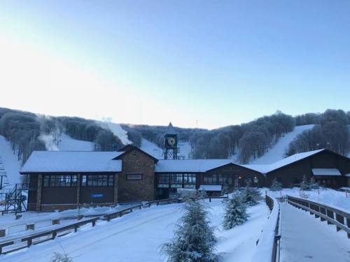 A snowy landscape featuring a ski resort building with a clock tower, surrounded by snow-covered hills and trees.