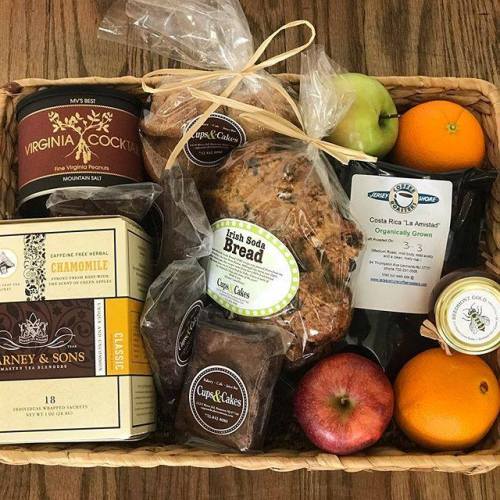 A wicker basket filled with snacks: bread, tea, an apple, and a jar of cocktail mix.