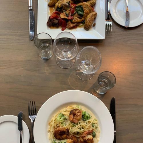 A table setting with two plates: one with shrimp pasta and broccoli, the other with chicken and vegetables.