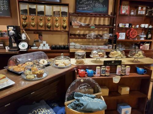 A cozy café display featuring various baked goods, coffee, and colorful tea canisters on wooden shelves.