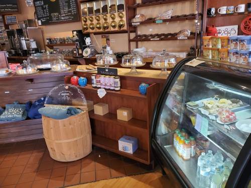 A cozy café display with pastries under glass domes, a drink fridge, and a wooden barrel in a warm, inviting atmosphere.