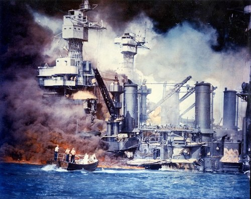 A naval ship engulfed in flames and smoke, with small boats nearby responding to the emergency.