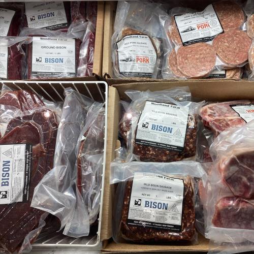 Packages of bison meat, including ground bison, sausage, and steaks, neatly arranged in cardboard boxes.