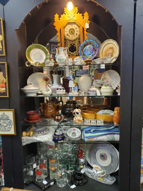 A display cabinet filled with various vintage dishes, glassware, and decorative items, including a clock and figurines.