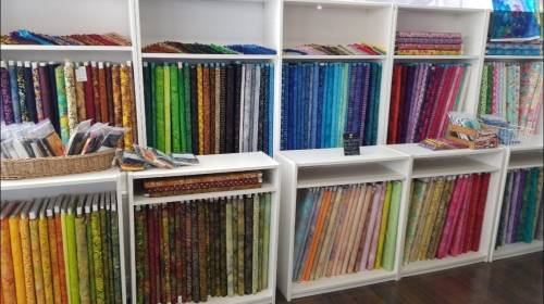 Colorful fabric rolls neatly arranged on shelves, showcasing a variety of patterns and textures in a craft store.