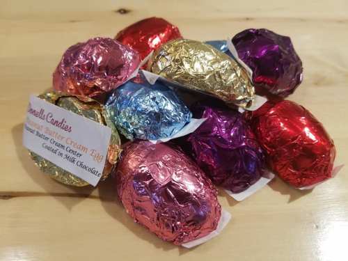A colorful assortment of foil-wrapped chocolate eggs with a label for "Peanut Butter Cream Egg" on a wooden surface.