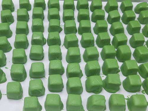 A grid of small, green, square-shaped candies arranged neatly on a white surface.