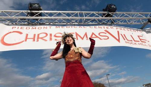 A woman in a festive outfit poses under a "ChristmasVille" banner against a blue sky.
