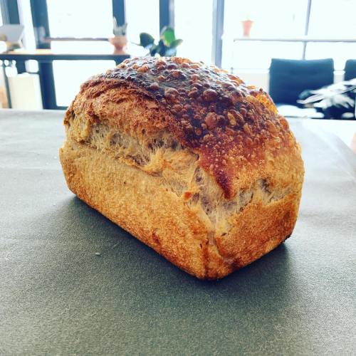 A freshly baked loaf of bread with a golden-brown crust, sitting on a table with a bright, airy background.