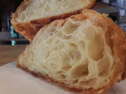 Close-up of a flaky, golden croissant cut in half, showcasing its airy, layered interior.