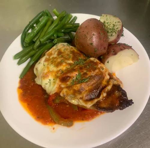 A plate of baked chicken topped with cheese, served with green beans, red potatoes, and marinara sauce.