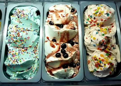 Three tubs of colorful gelato: mint with sprinkles, vanilla with chocolate sauce and berries, and creamy vanilla with candy.