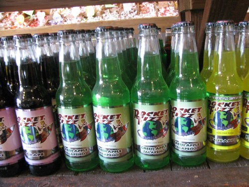 A row of colorful soda bottles labeled "Rocket Fizz," featuring flavors like green apple jalapeño and grape.