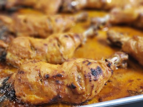 Close-up of golden-brown roasted chicken drumsticks in a savory sauce on a baking tray.