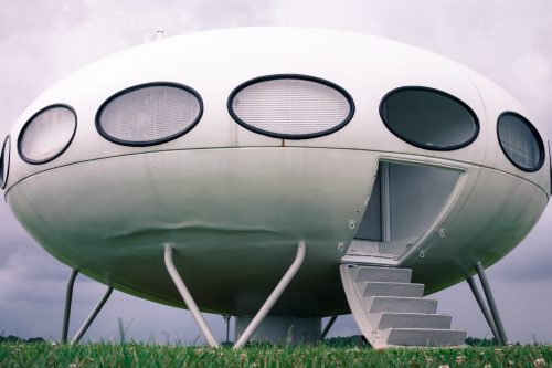 A futuristic, oval-shaped building with large circular windows and a staircase, set against a cloudy sky.