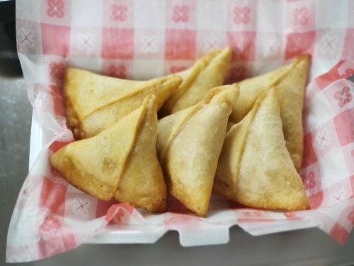 A basket of golden-brown samosas arranged neatly on a red and white checkered paper.