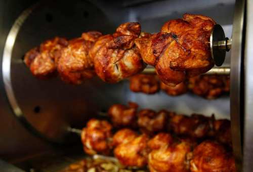 Rotisserie chickens cooking on a spit, golden brown and crispy, in a commercial rotisserie oven.