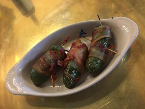 Three bacon-wrapped jalapeño peppers on a white dish, secured with toothpicks, resting on a golden surface.