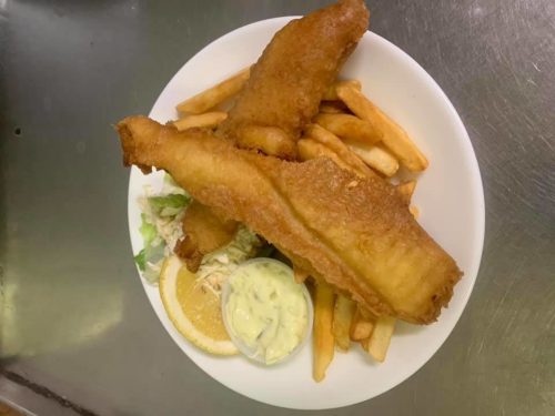 A plate of golden-brown fried fish fillets, French fries, coleslaw, and a lemon slice with tartar sauce.