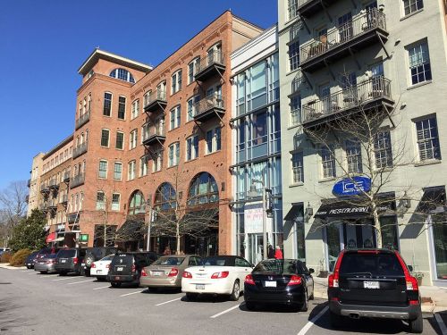 A street view of a mixed-use building with shops and apartments, featuring parked cars and clear blue skies.