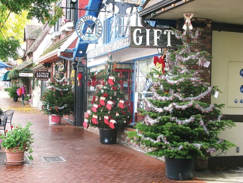 A festive street scene with decorated Christmas trees and shops adorned with holiday decorations.