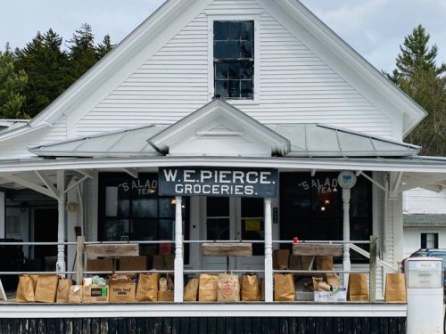 A white grocery store with a sign reading "W.E. Pierce Groceries," featuring bags of goods on the porch.