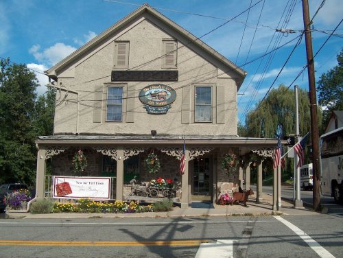 Historic building with a porch, decorative trim, and American flags, featuring a sign for a local business.