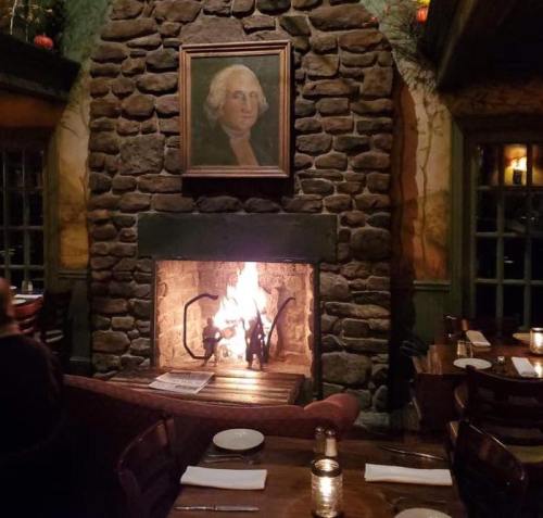 Cozy restaurant interior featuring a stone fireplace, a portrait of George Washington, and candlelit tables.