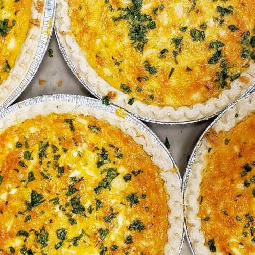 Four freshly baked quiches with golden crusts, topped with herbs and a cheesy filling.