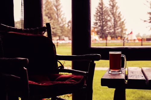 A cozy scene featuring a chair and a mug of beer on a table, with a view of trees and a playground outside.
