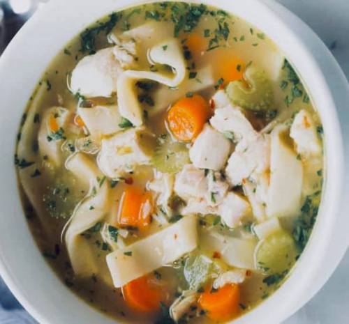 A bowl of chicken noodle soup with carrots, celery, and herbs in a savory broth.