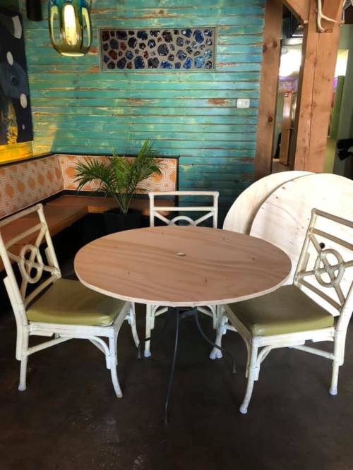 A round wooden table with two white chairs in a colorful restaurant setting, featuring green walls and decorative accents.