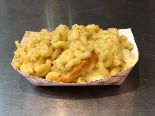 A serving of creamy macaroni and cheese in a paper tray, featuring curly pasta and a golden, crispy topping.