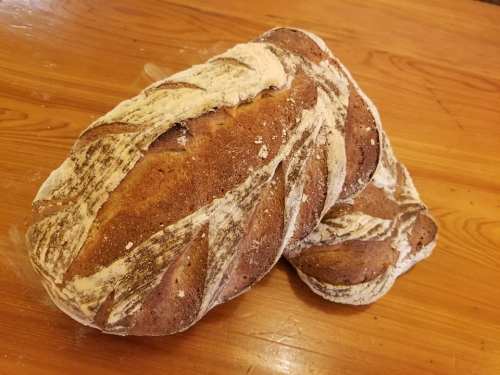 Two loaves of freshly baked bread with a rustic crust, resting on a wooden surface.