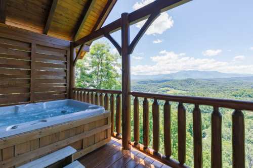 A hot tub on a wooden deck with a scenic mountain view and blue sky in the background.