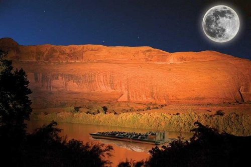 A boat on a river under a bright full moon, with illuminated cliffs in the background at night.