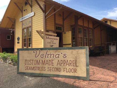 A yellow building with a sign for the Brownsville Museum and a sign for Velma's Custom-Made Apparel on the second floor.