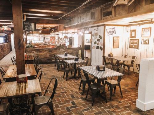 A rustic dining area with wooden tables, metal chairs, and brick flooring, featuring warm lighting and decor.