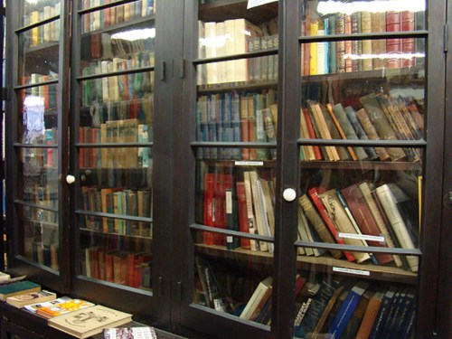 A wooden bookshelf filled with various books, some visible through glass doors, showcasing a mix of colors and sizes.