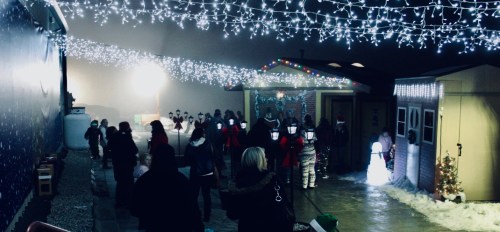 A festive outdoor scene with people enjoying holiday lights and decorations in a snowy setting.