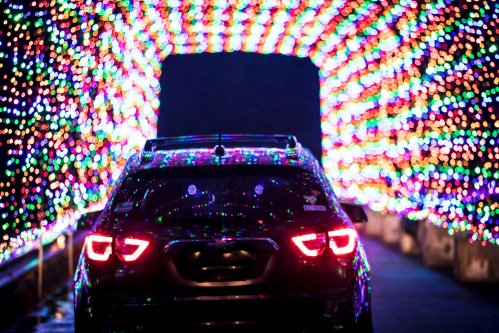 A car drives through a colorful tunnel of bright, twinkling holiday lights.