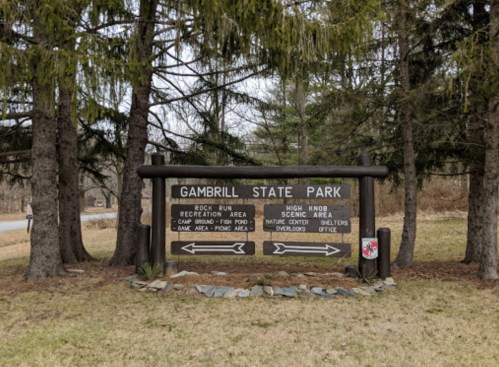 Sign for Gambrill State Park with directions to various areas, surrounded by trees and grass.