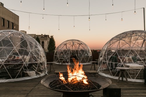 Cozy outdoor space with transparent domes, a fire pit, and string lights at sunset.