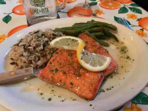 Grilled salmon fillets with lemon, served with wild rice and green beans on a colorful tablecloth.